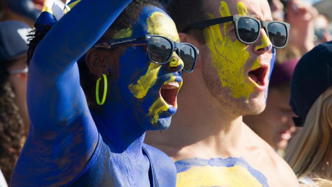 a male and female student painted in UC Davis blue and gold cheer on the Aggies at the annual homecoming football game