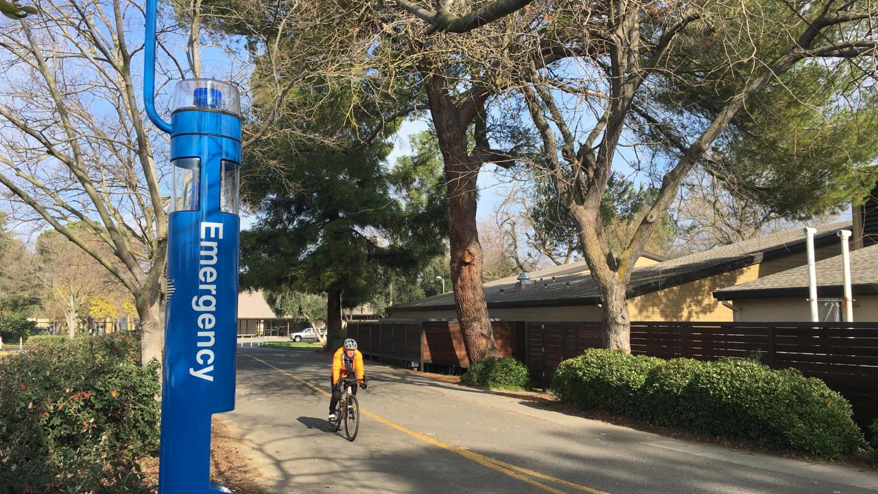 Blue-light emergency call station along Sprocket Bikeway, with bicyclists passing by