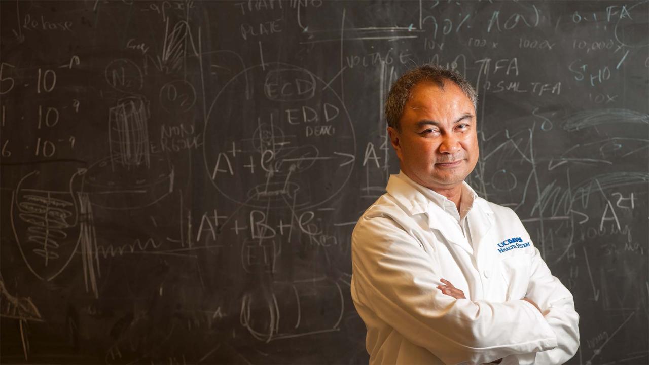 Photo of person in lab coat standing in front of chalkboard