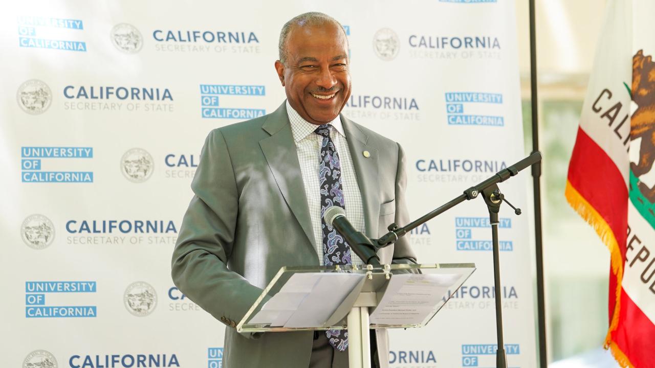 Chancellor in suit and tie at lectern, smiling