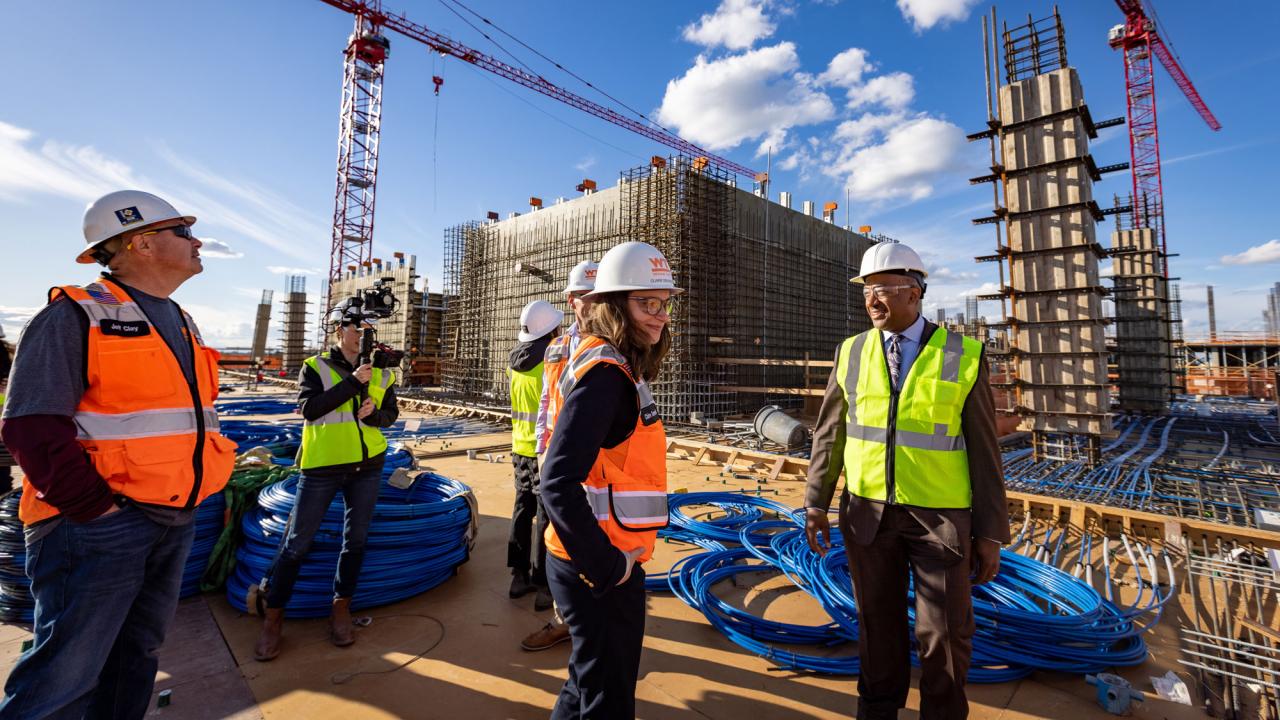 Chancellor May in hard hat and yellow vest atop Aggie Square construction, cranes in background