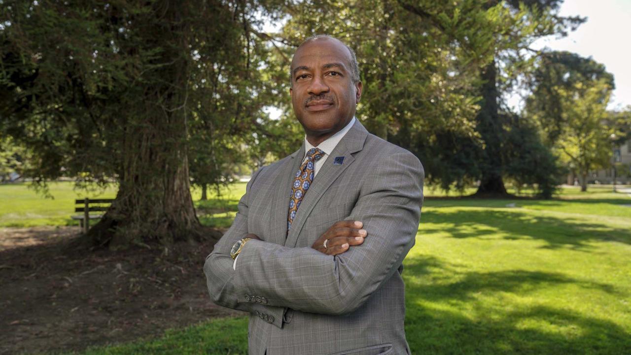 Chancellor Gary S. May stands in front of a tree on the Quad, with his arms crossed.
