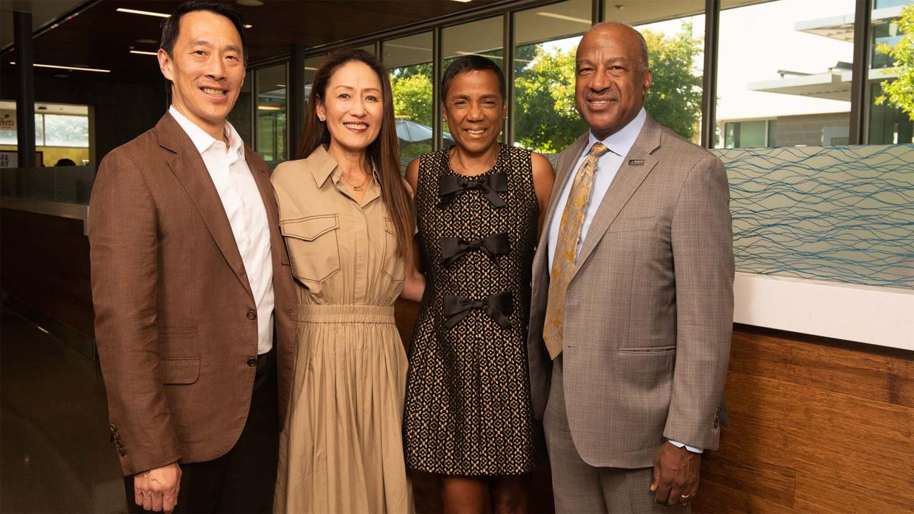 Group photo of four smiling adults in business attire standing indoors by a window