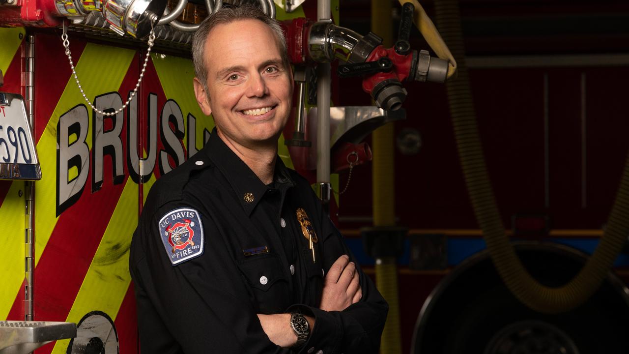 Fire chief stands in front of a fire truck with arms crossed.