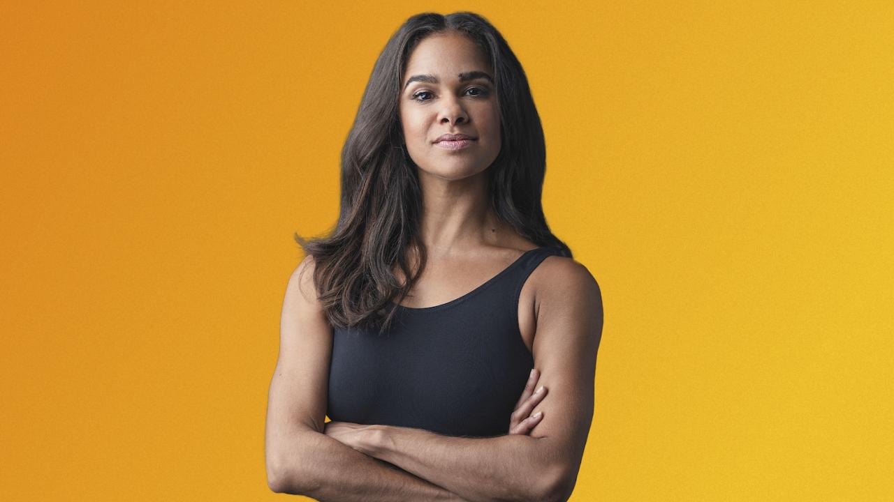 Misty Copeland smiling wearing black top and crossing arms in front of yellow background