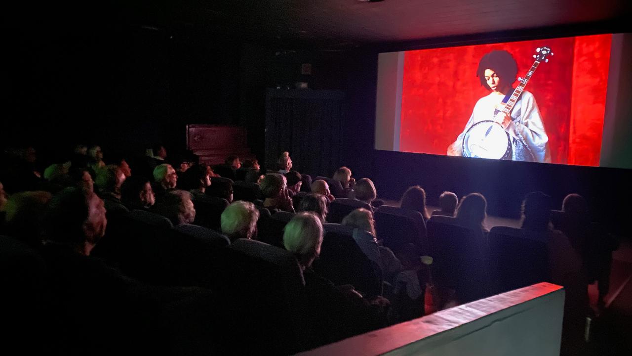 Insidea dark theater, on screen someone plays a banjo