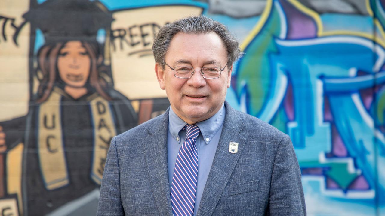 Man in dark suit in front of mural 