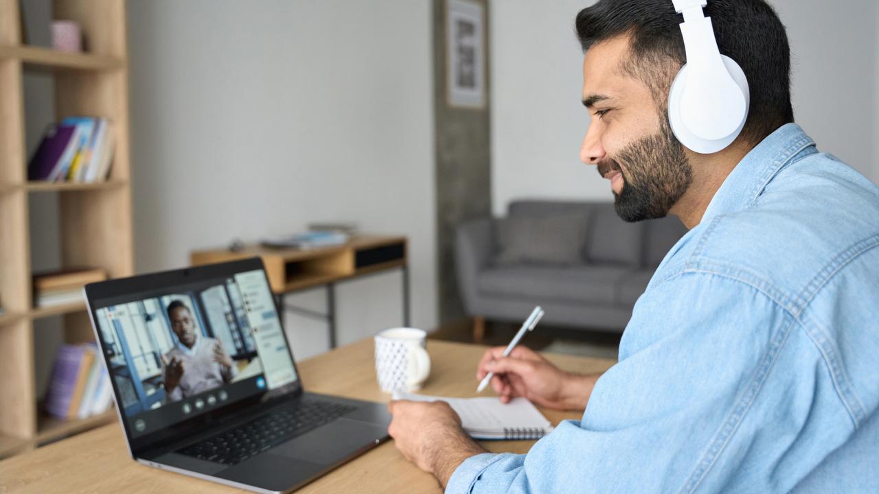 A man wearing headphones listens to someone on a computer screen