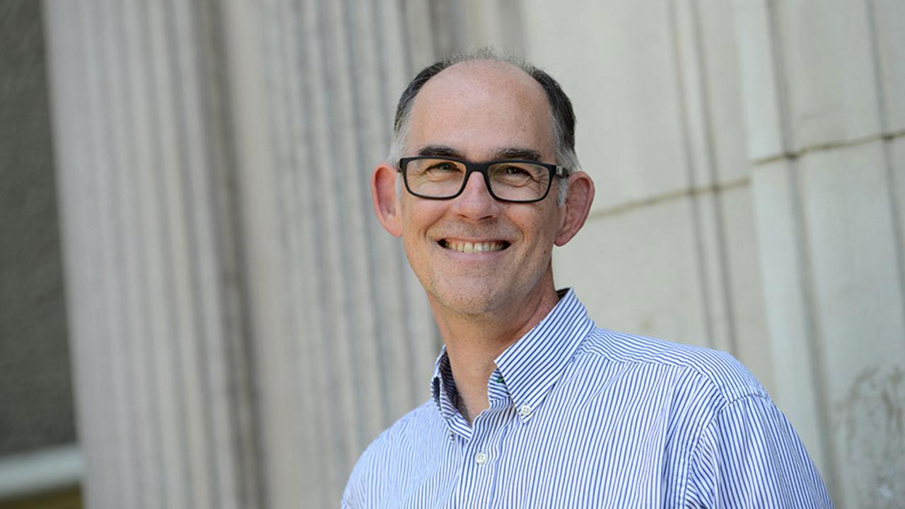 Smiling man with glasses in blue shirt standing by stone columns