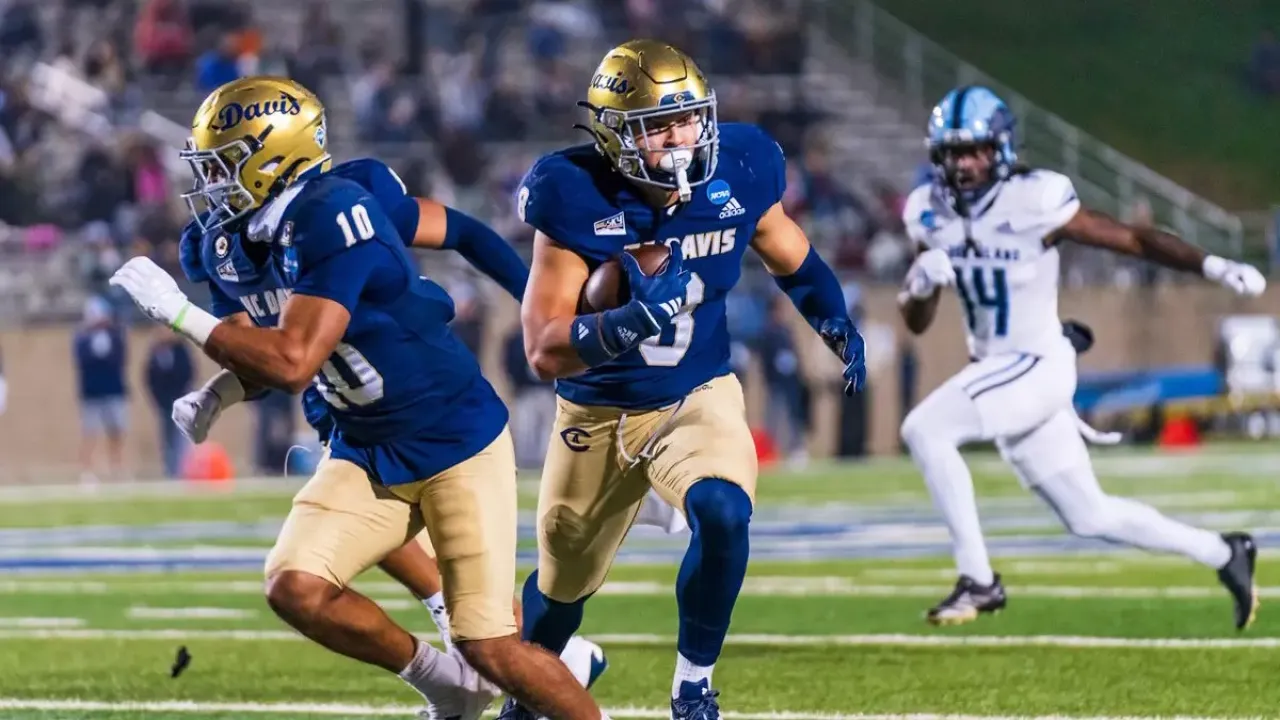 Football players in blue and gold; ball carrier runs as teammate blocks, white defender pursues
