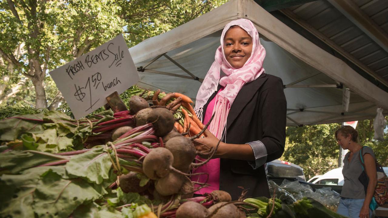 A female student picks up some veggies at the Davis Farmer's Market