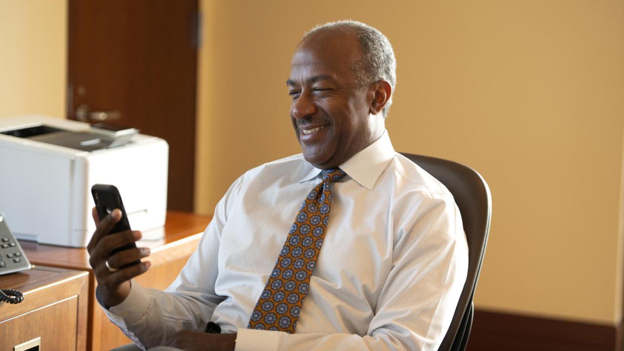 Chancellor Gary S. May, in shirt and tie, smiling, looking at phone.