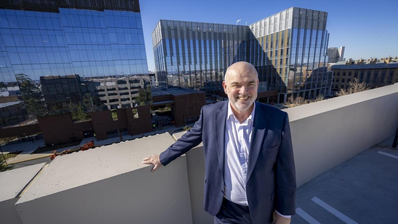 George Baxter poses for photo with Aggie Square buildings in background.
