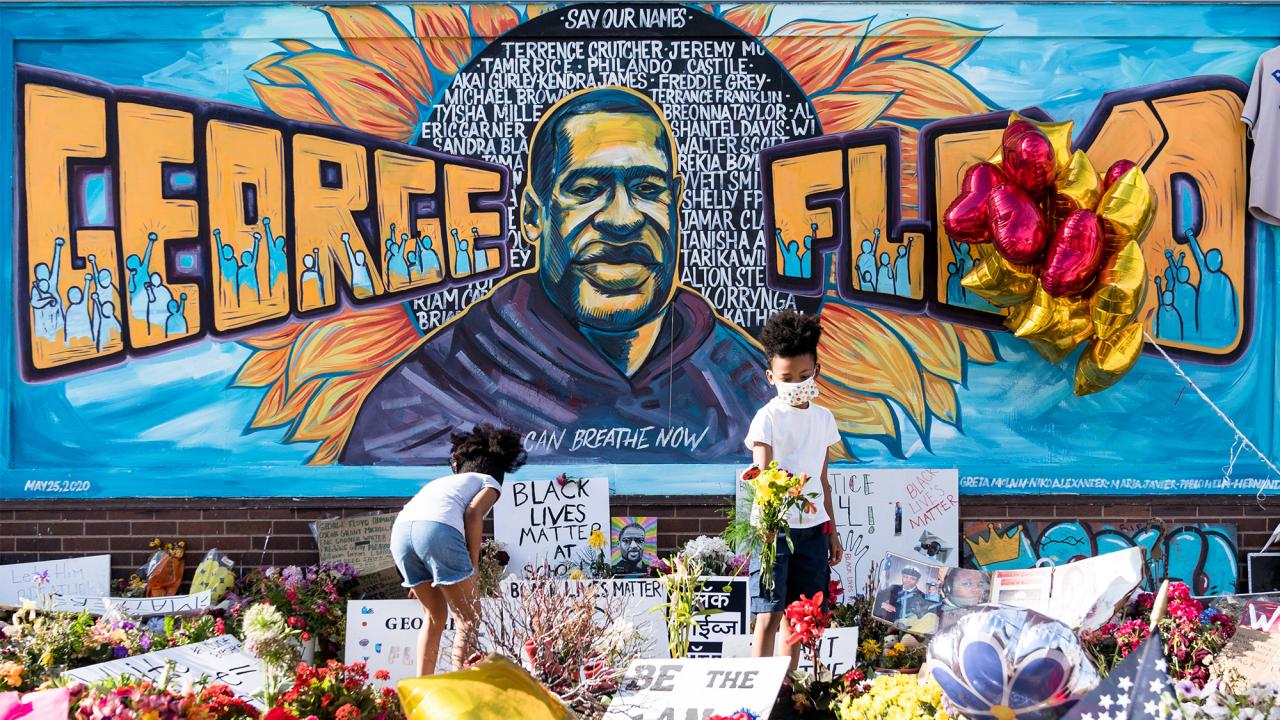 Children place flowers in front of mural dedicated to George Floyd.