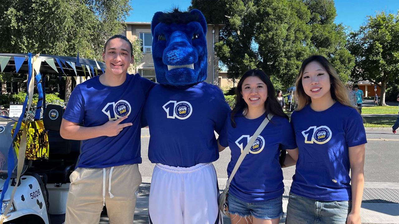Three people smiling with Gunrock mascot outdoors, wearing blue shirts with 10 logo