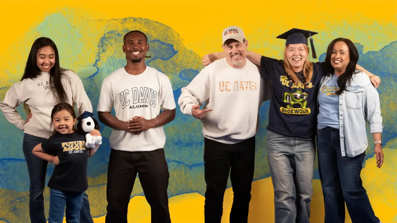 Smiling diverse group of six in a photo, one wearing a graduation cap, against a colorful backdrop