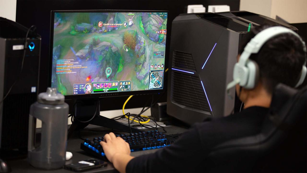 Person wearing headset plays multiplayer PC game at desktop with lit tower and water bottle