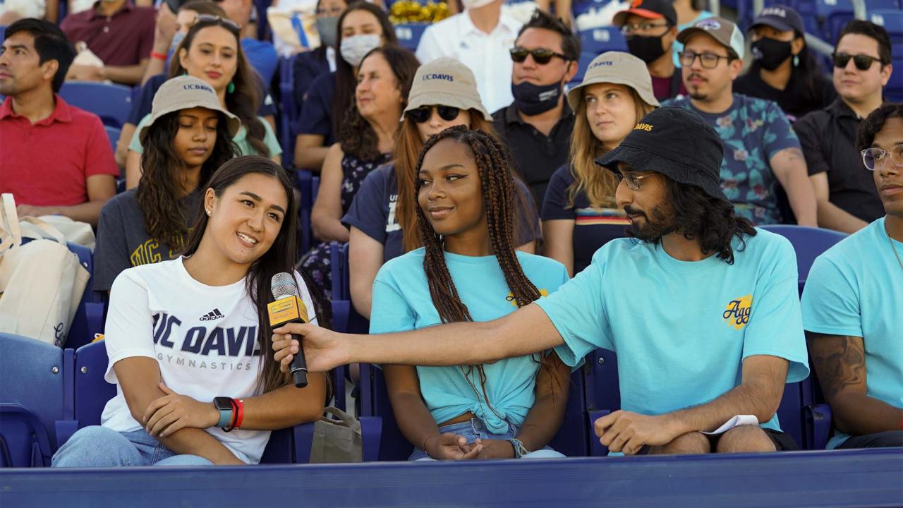 Student speaks into microphone while sitting in stadium crowd.