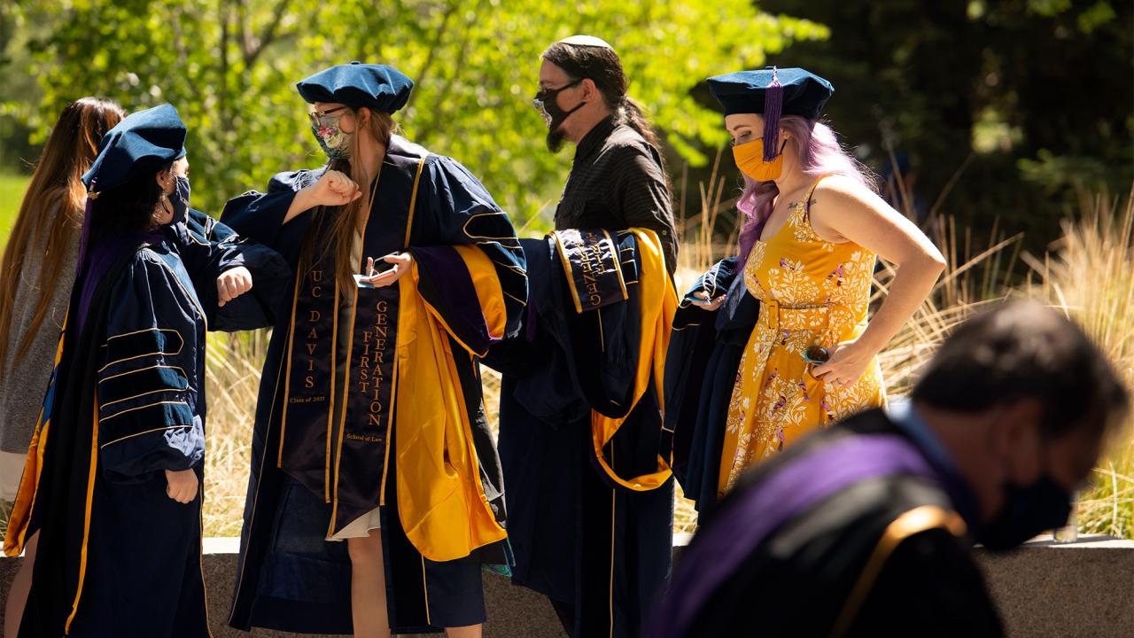 Law graduates greet each other by bumping elbows.