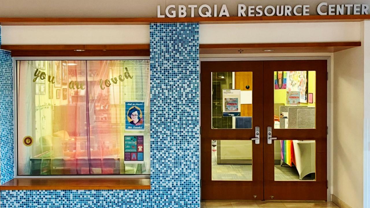 LGBTQIA Resource Center window with rainbow curtain, wooden double doors, blue mosaic tiles