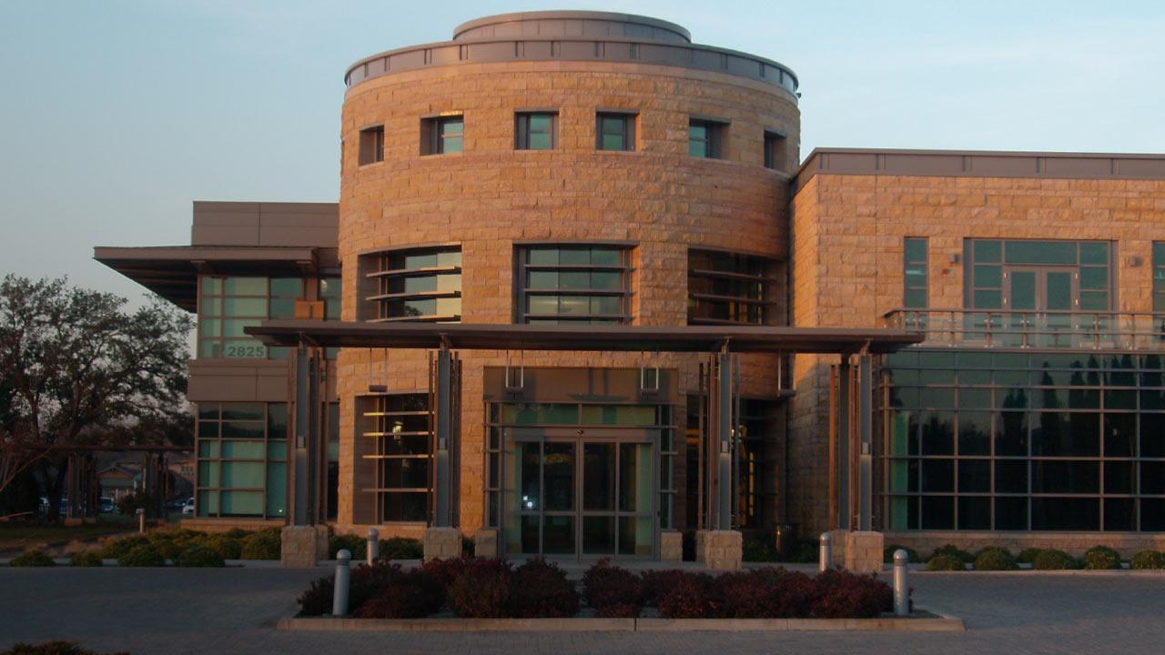 Exterior of a reddish modern two-story building lit by evening light. 