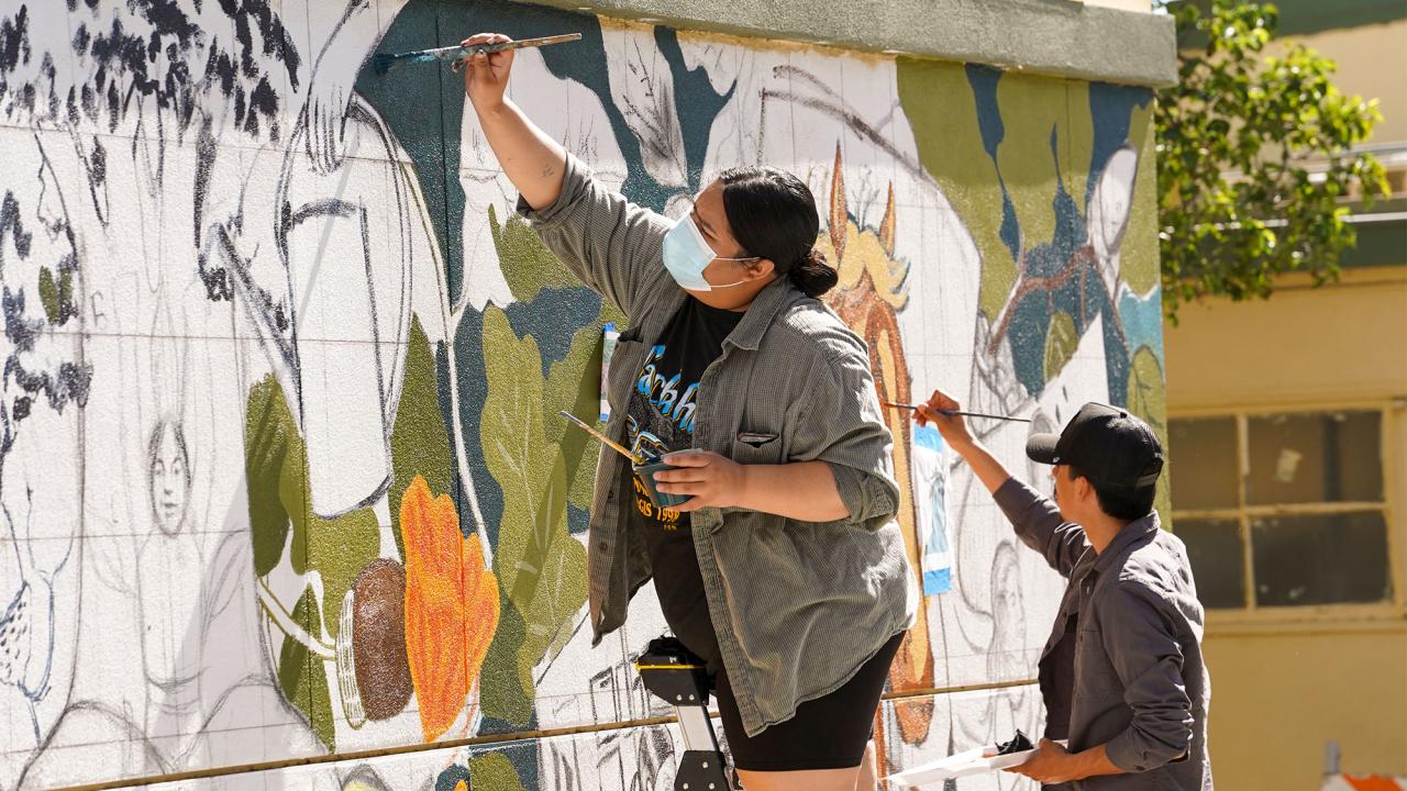 Two students paint a mural at a school