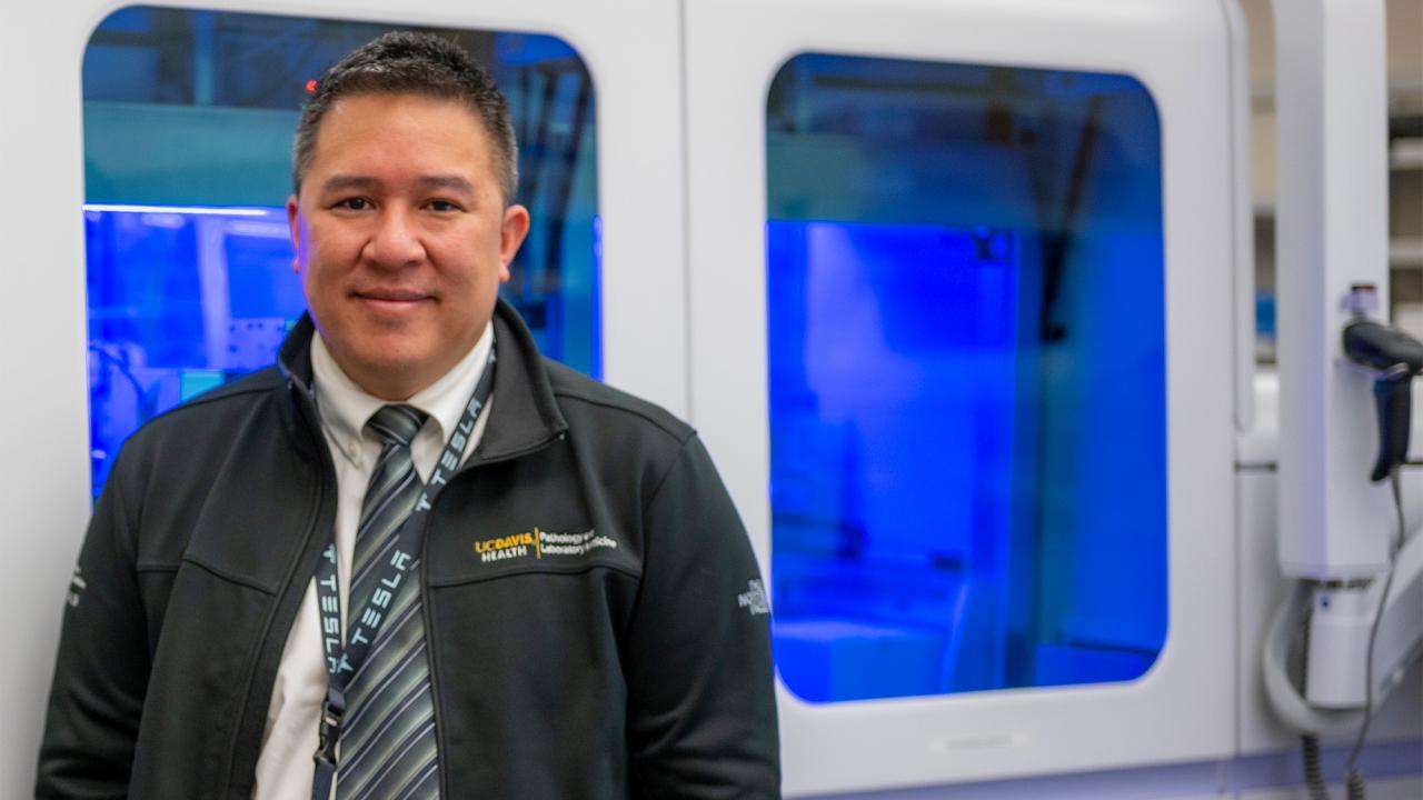 A man stands in front of a mechanized laboratory machine that processes medical samples.