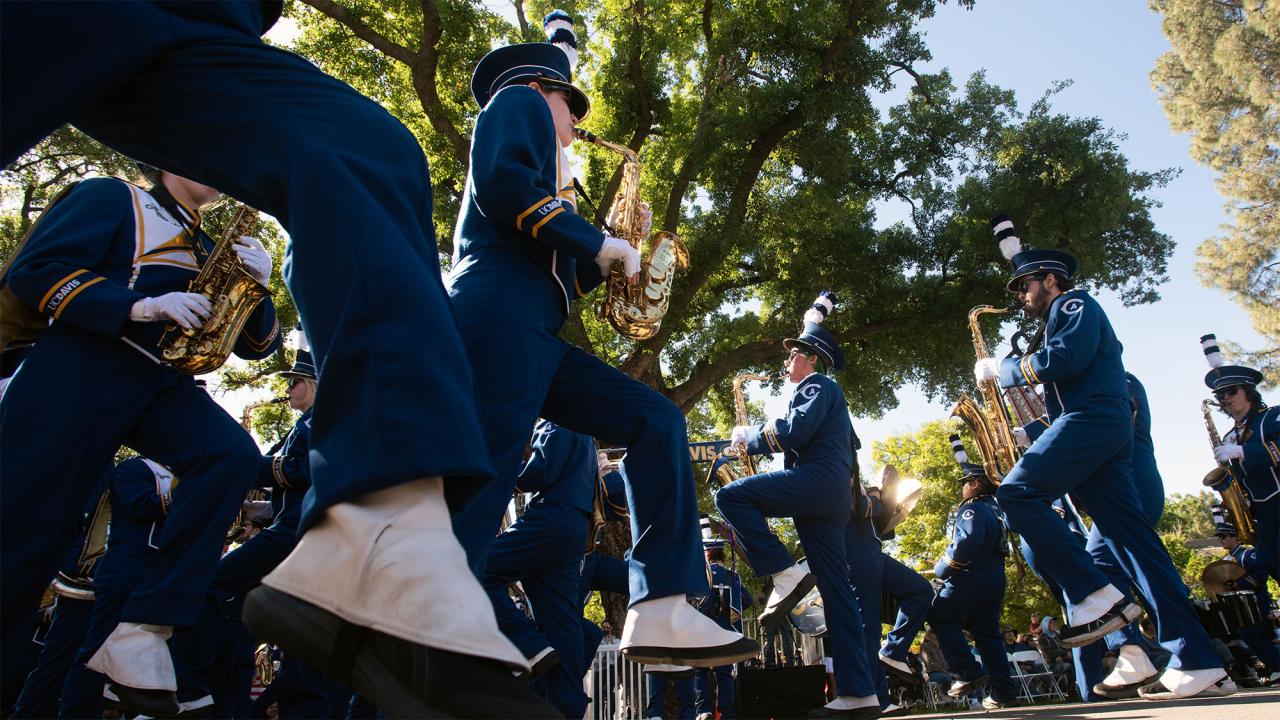 Low-angle of marching band in navy uniforms and white shoes stepping under sunlit trees