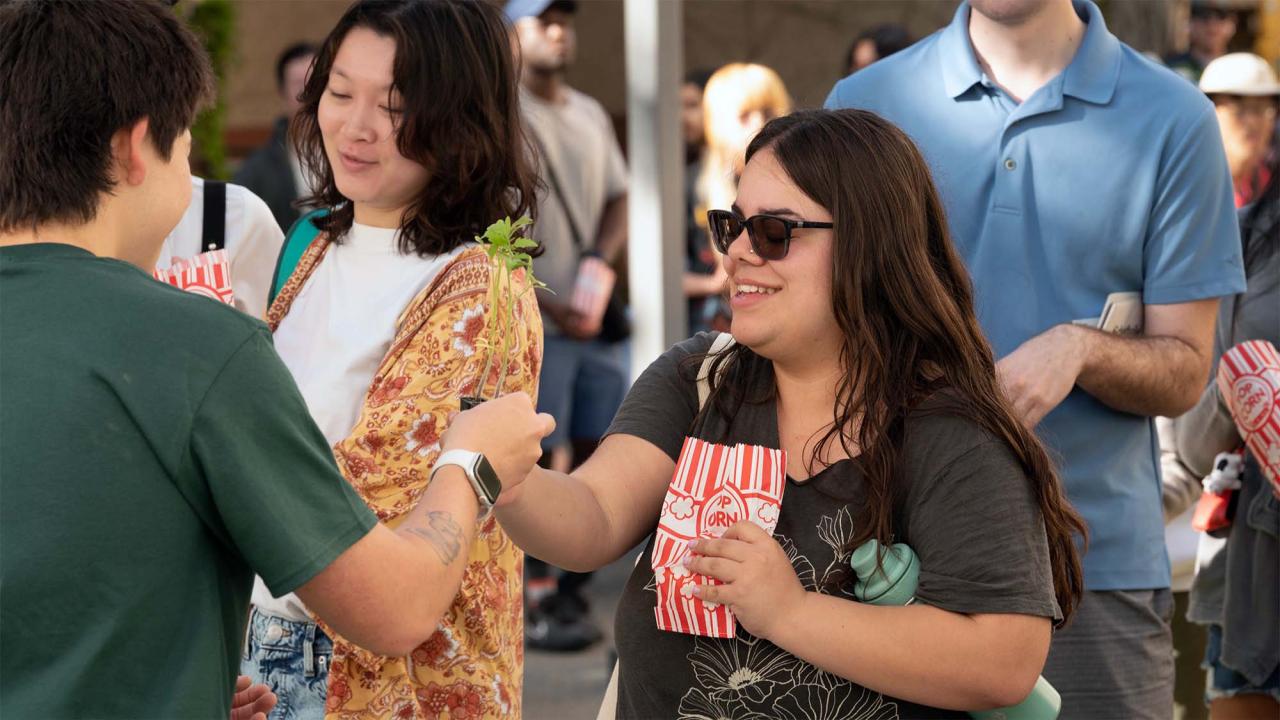 Smiling woman in sunglasses holding popcorn at a crowded outdoor gathering