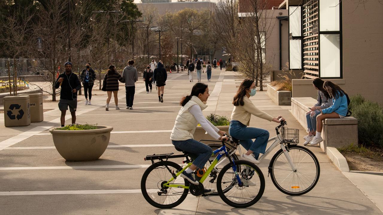 Two women biking with the promenade in the background