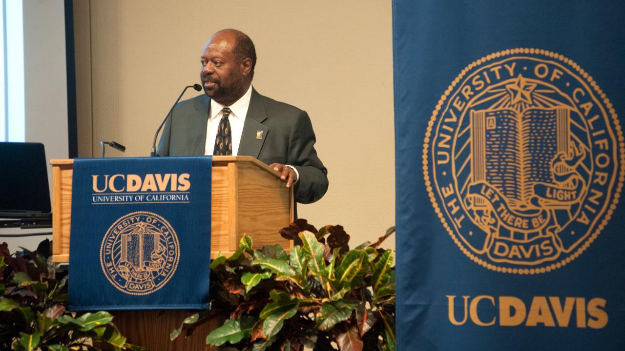 Rahim Reed speaks at podium with UC Davis banners on podium and behind him.