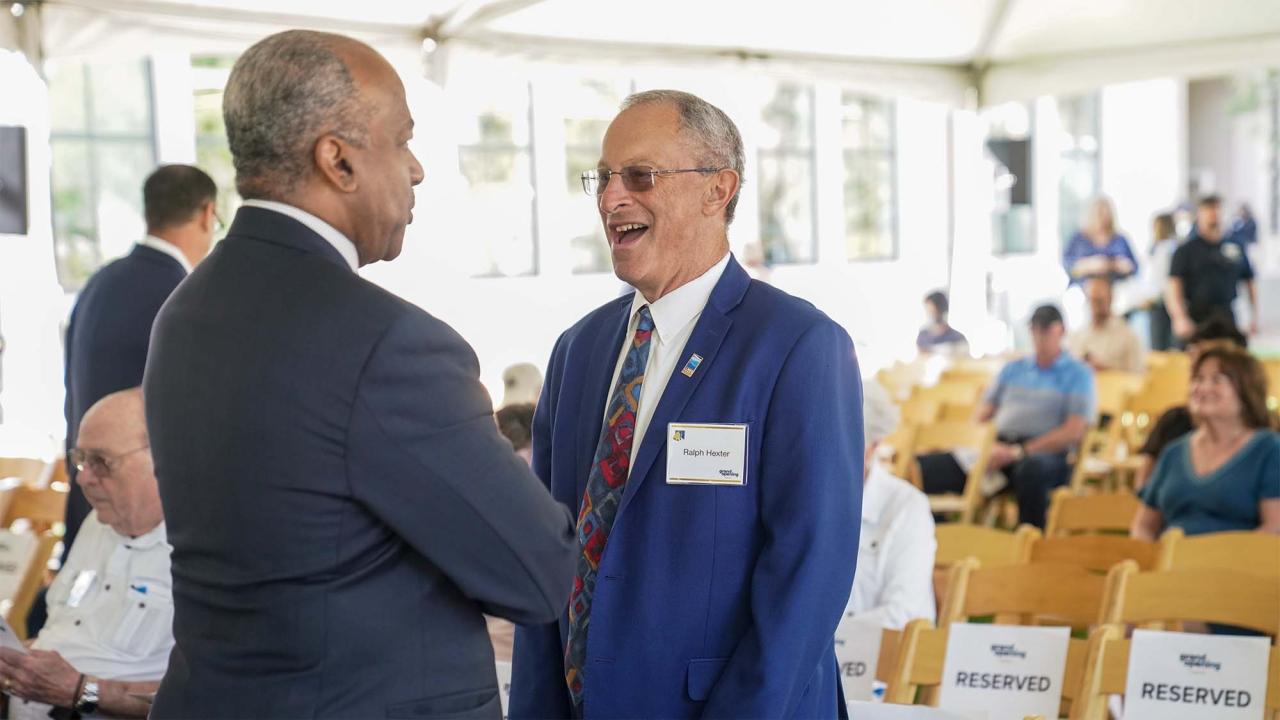 Two men in suits smiling and shaking hands at an indoor event; candid photograph.