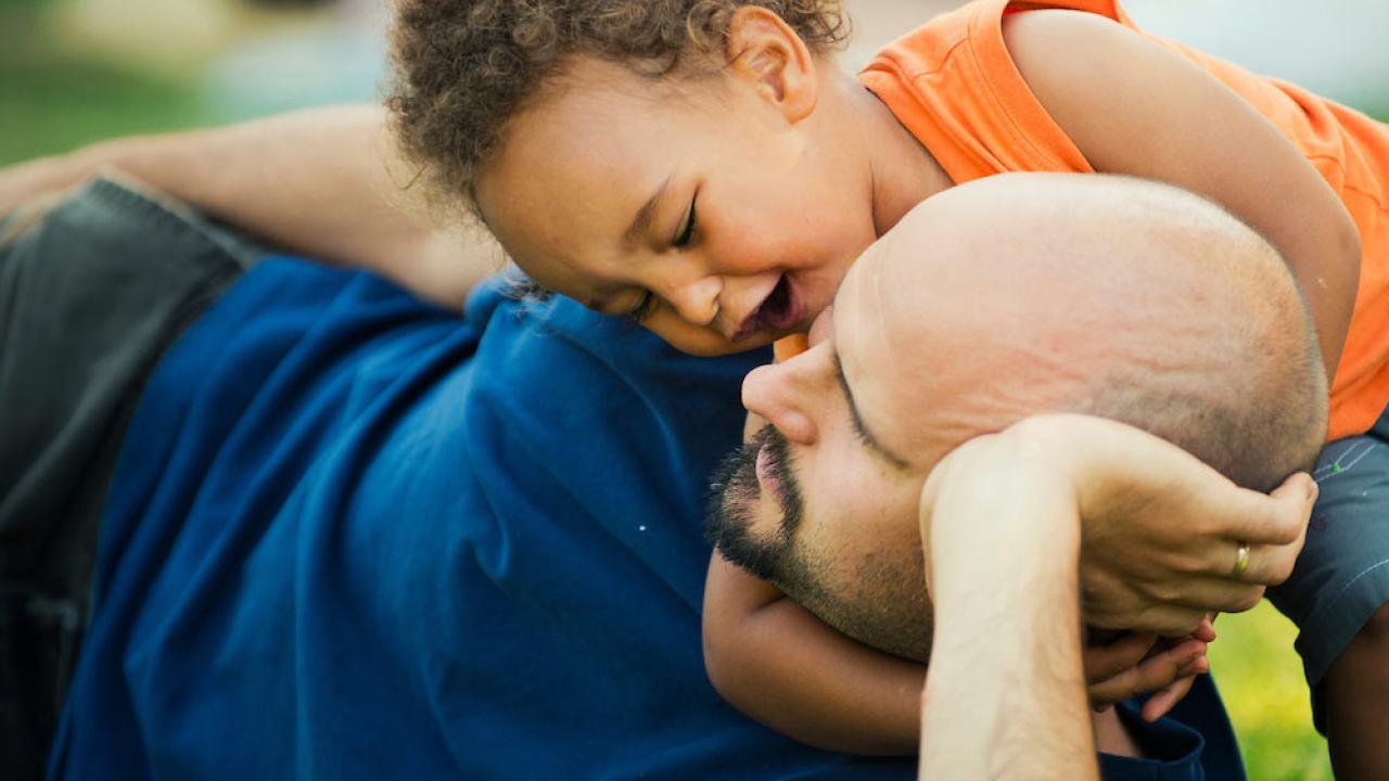 a toddler plays with his dad on the grass in Davis's central park