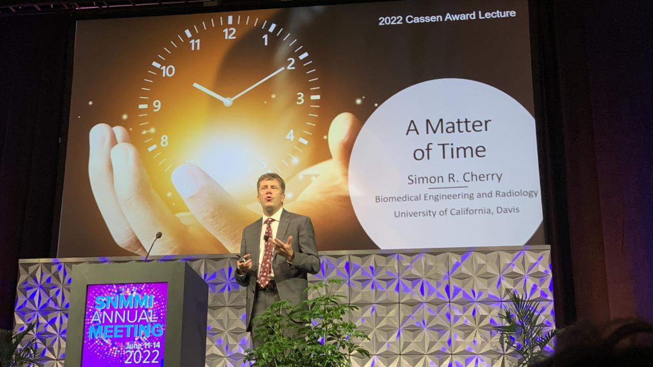 Distinguished Professor Simon Cherry delivers lecture in front of title slide, "A Matter of Time"