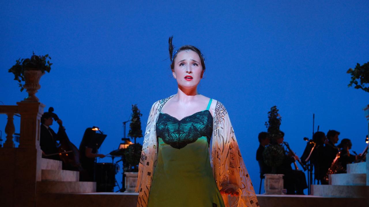 Woman on theatre stage, in costume, with blue-lighted background