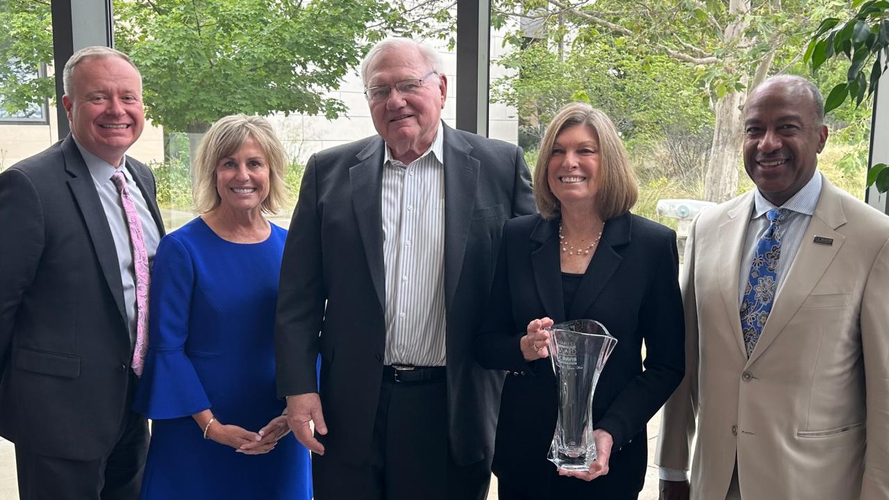 Five people pose, in a line, one holding glass trophy