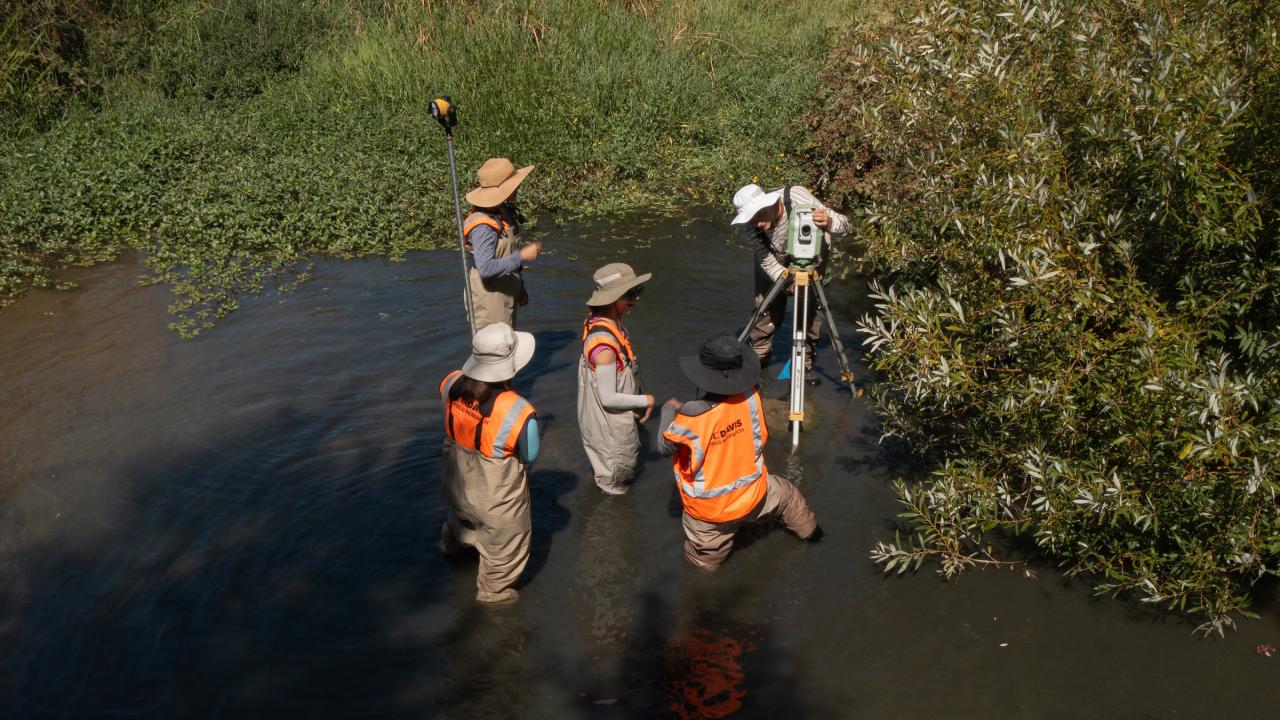 UC Davis researchers photographed from above a creek conduct a stream survey in the water wearing bright orange vests