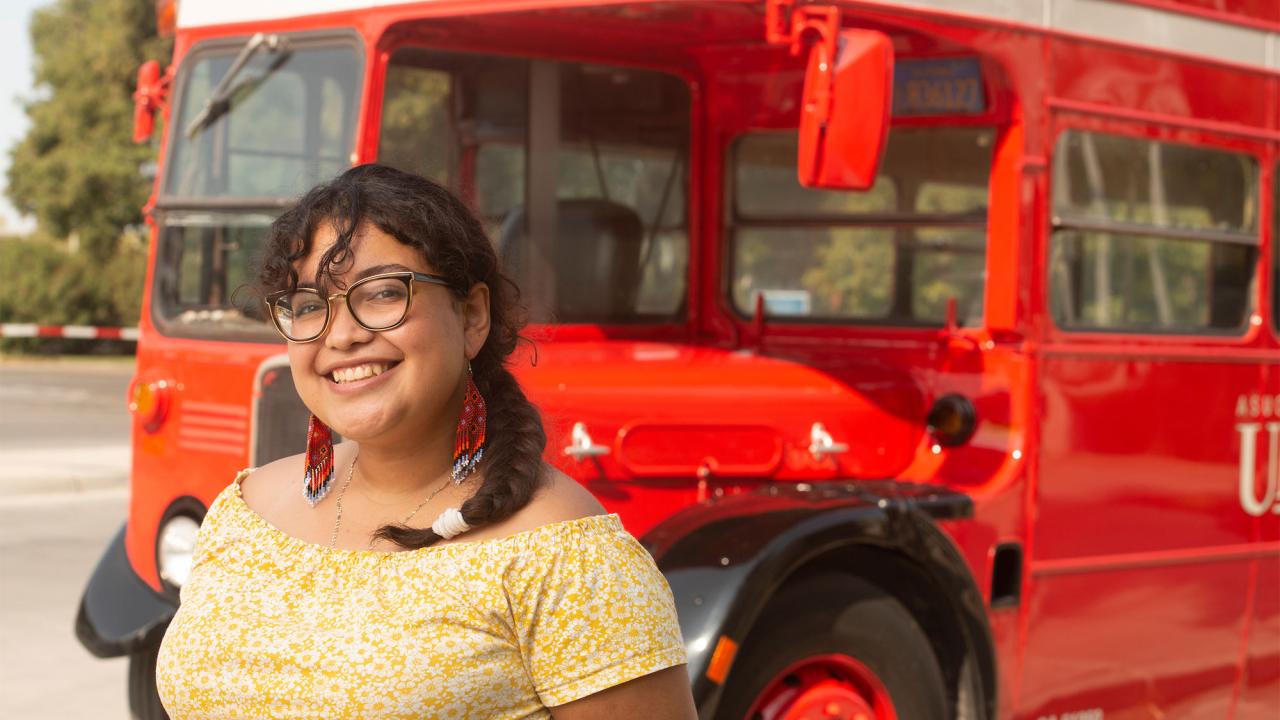 A female student stands in front of a double-decker Unitrans bus