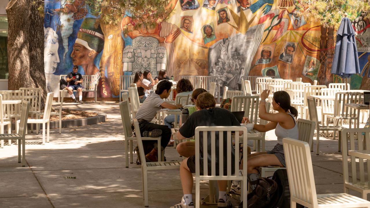 Students studying on UC Davis campus on white tables and chairs in front of mural