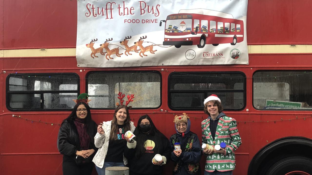 Five people stand against the side of a Unitrans double-decker bus