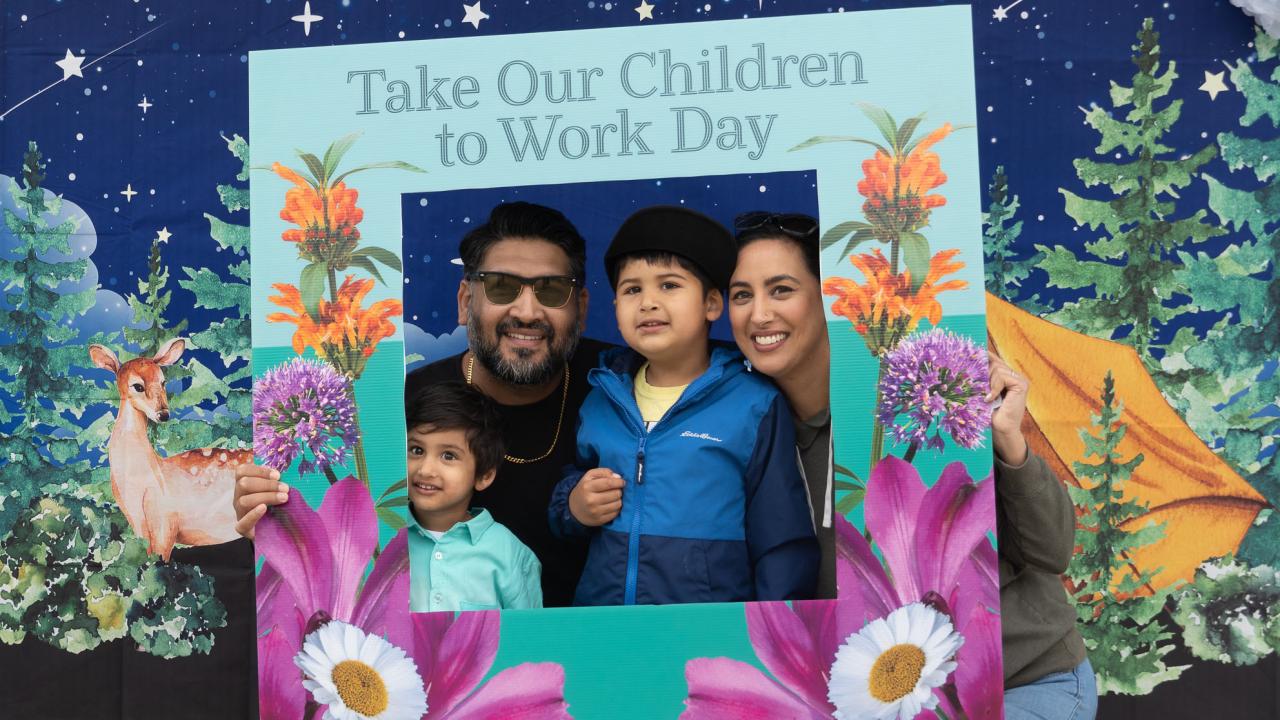 Smiling family posing in floral "Take Our Children to Work Day" event frame