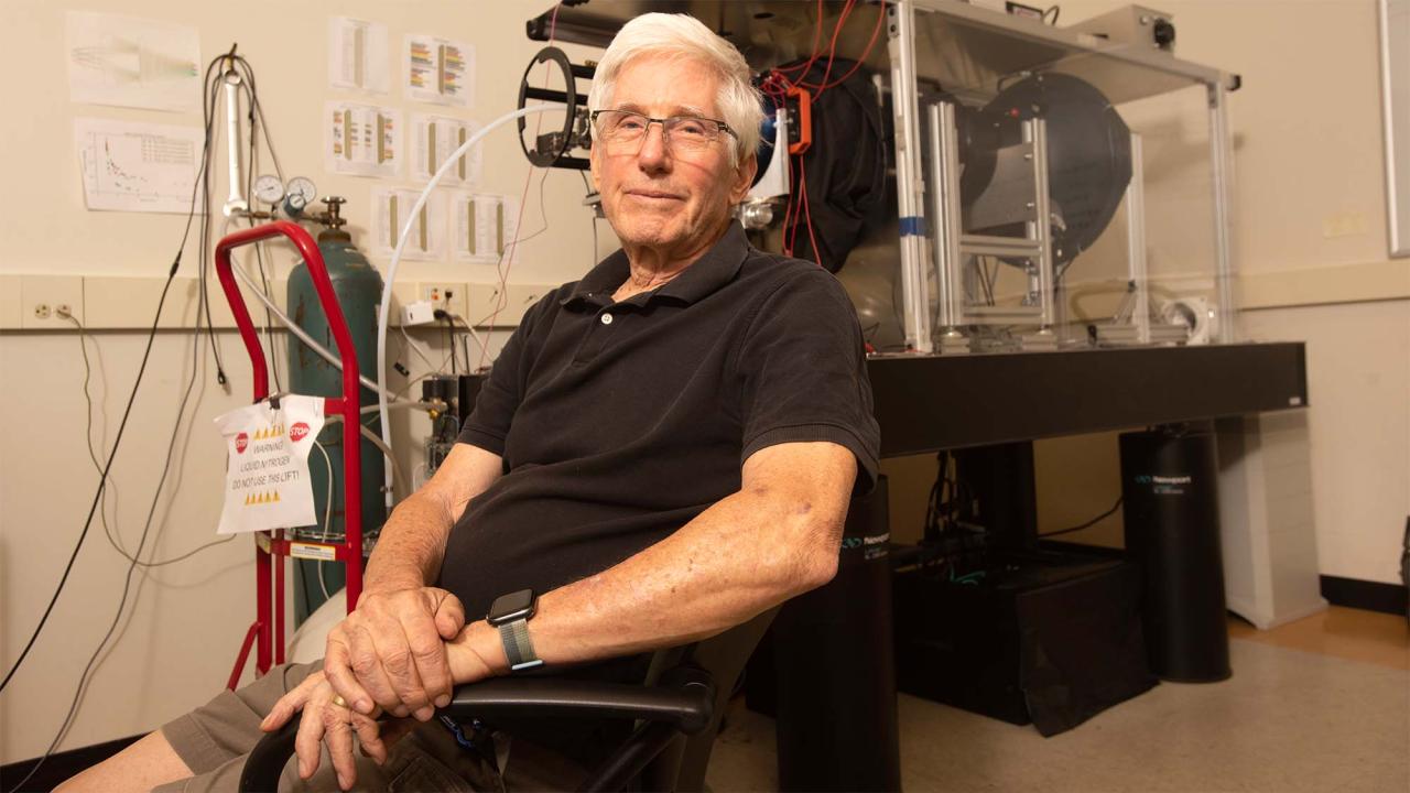 Man smiling, seated in lab with equipment
