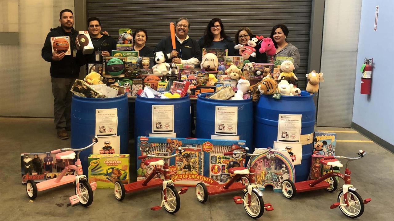 Group of people stand in front of large pile of new toys and tricycles collected during a toy drive.