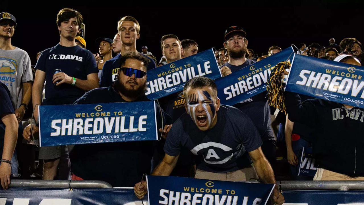 Energetic fans in blue shirts holding SHREDVILLE signs, man shouting in stadium photo