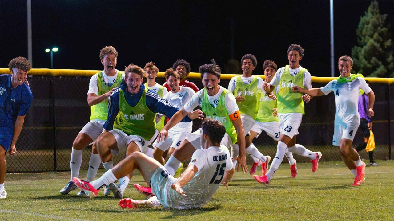 Youth soccer players cheering on lit field at night; goalkeeper on ground