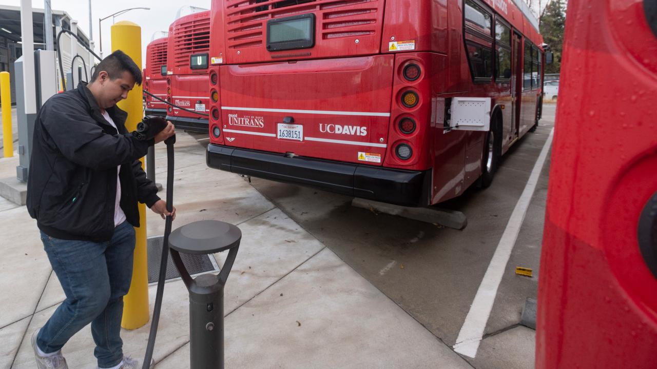 Person handles charging cable in bus yard with red buses