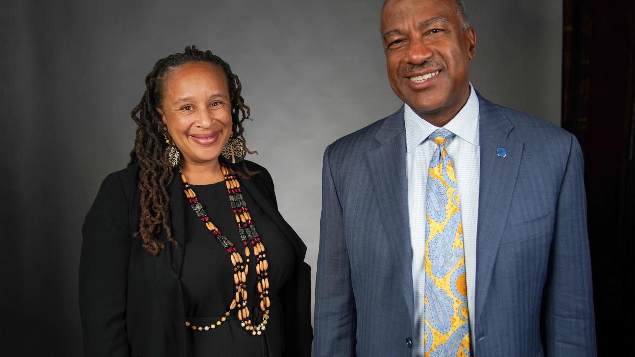 Against a black backdrop inside a recording studio, Professor Beth Rose Middleton, standing on the left, is next to Chancellor Gary S. May.