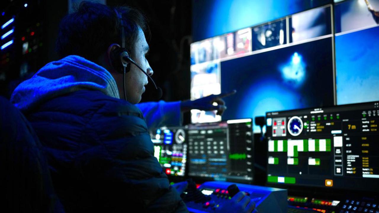 Man with headset with blue-lit monitors and tech gear