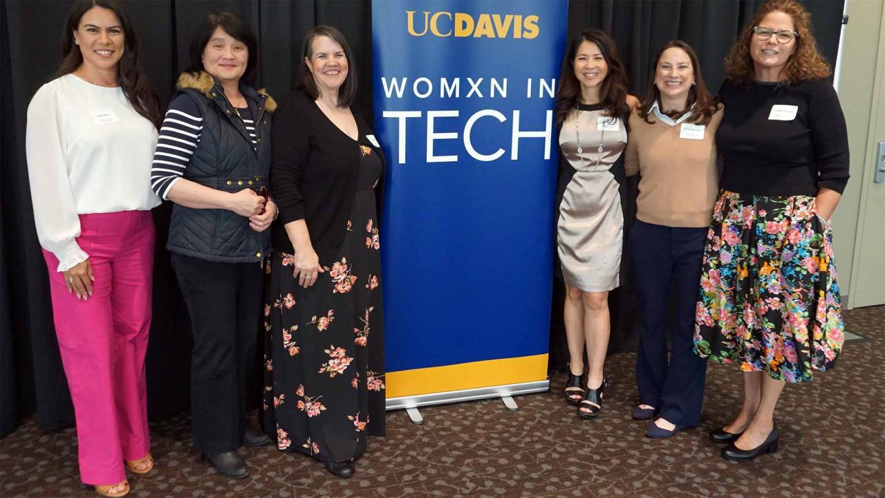 Six people pose for photo in front of banner