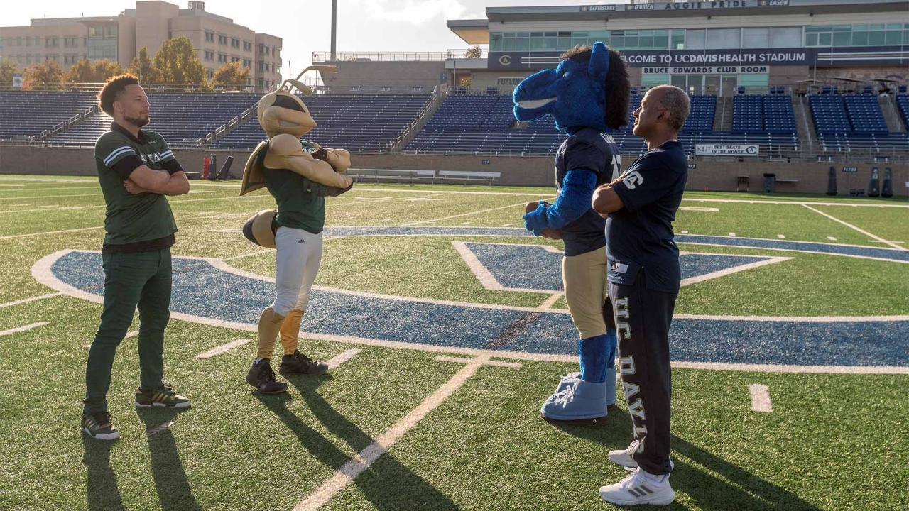 Luke Wood and Gary S. May stand across from each other on the football field, with Herky and Gunrock behind them.